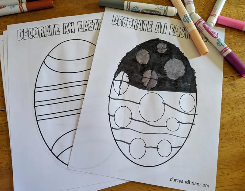 Printed Easter egg coloring sheets on table by markers. One egg is partially colored in.