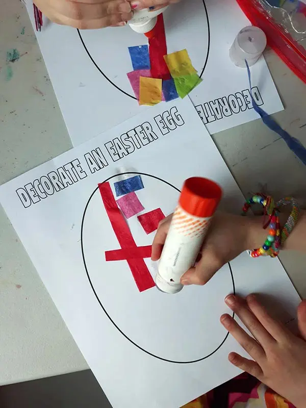 Kids gluing pieces of colored tissue paper to blank egg template.