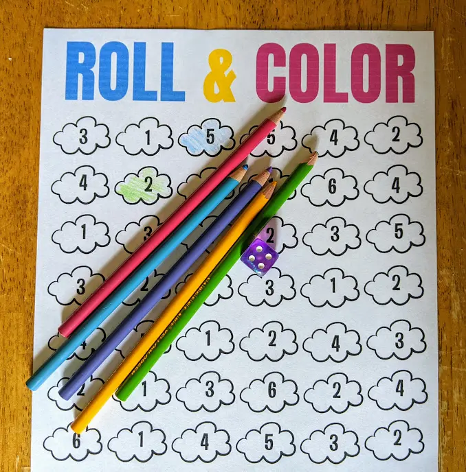 Cloud roll and color math game printed out and set on wooden table with colored pencils and six sided die.