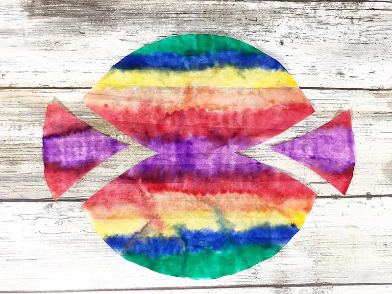 Rainbow colored coffee filter laid flat, showing circle shape with triangle section cut out from each side.