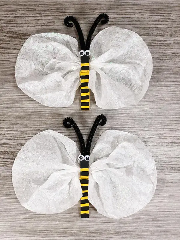 Overhead view of two finished coffee filter bees laying vertically on gray wood background.