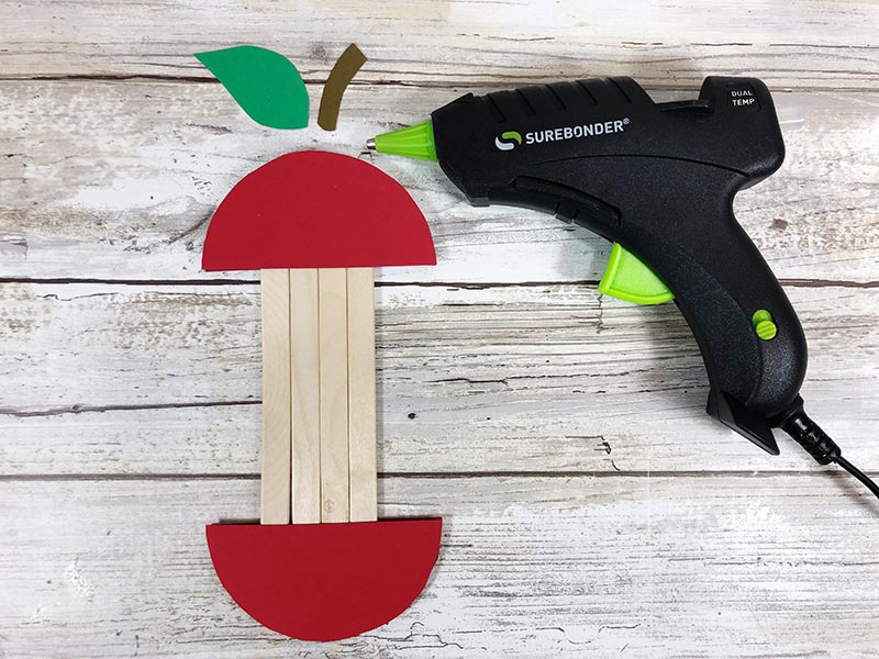 Using glue gun to attach cardstock stem and leaf to top of apple craft.