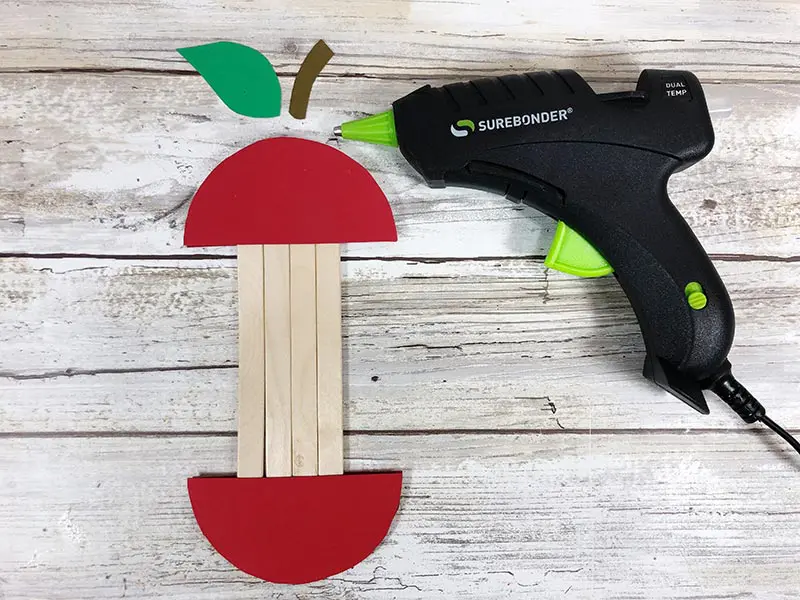 Using glue gun to attach cardstock stem and leaf to top of apple craft.