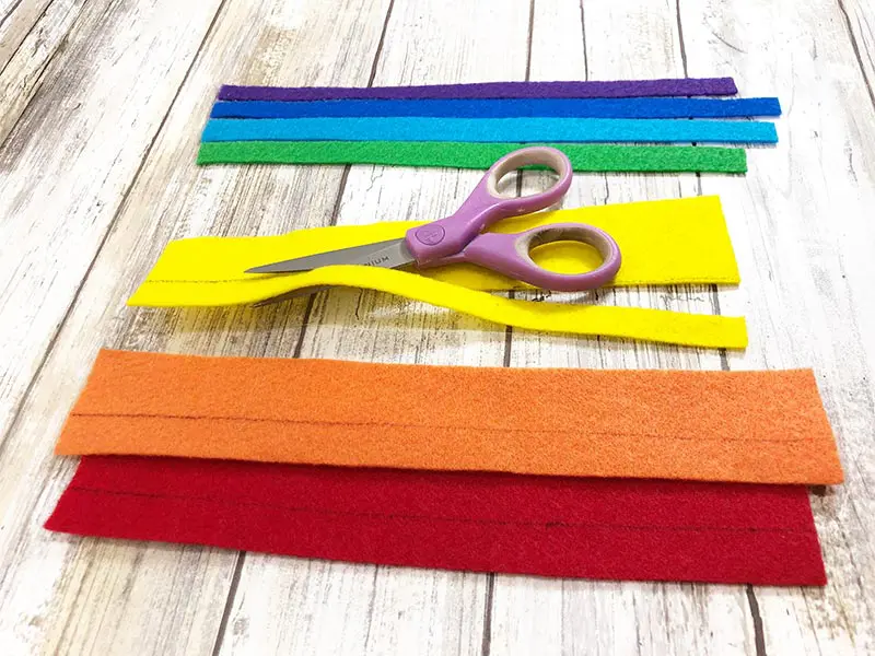 Scissors cutting strips of craft felt in assorted colors of the rainbow.
