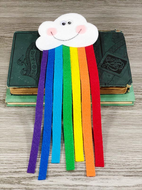 Completed felt rainbow cloud with Kawaii smiley face laying on top of stack of closed books.