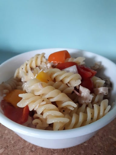 White bowl with Italian pasta salad on table in front of light blue wall.