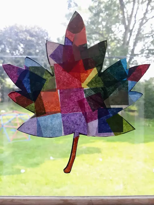 Finished multi-colored tissue paper leaf suncatcher craft hanging in sunny windown.