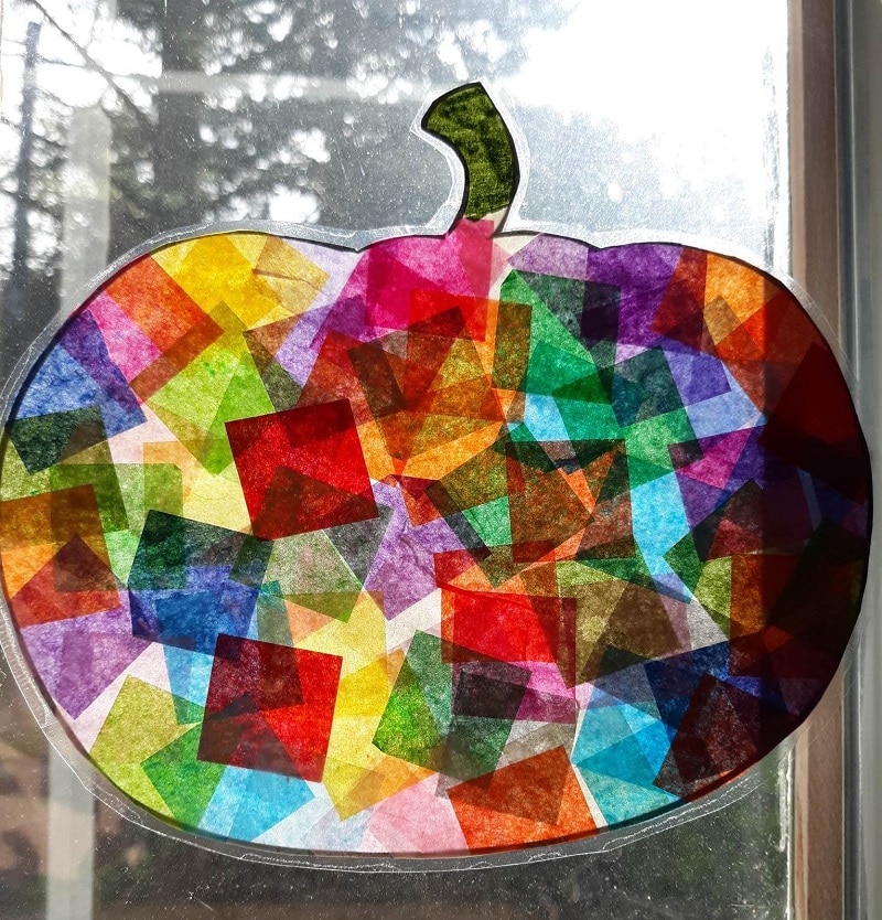 Close up of sun shining through tissue paper pumpkin suncatcher hanging in window.