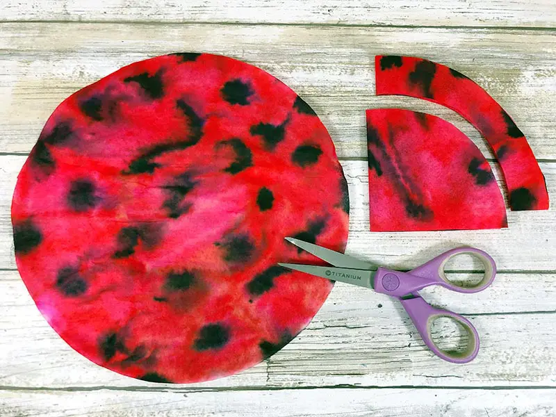 One round coffee filter colored like a ladybug and scissors laying next to folded coffee filter showing how to trim it.