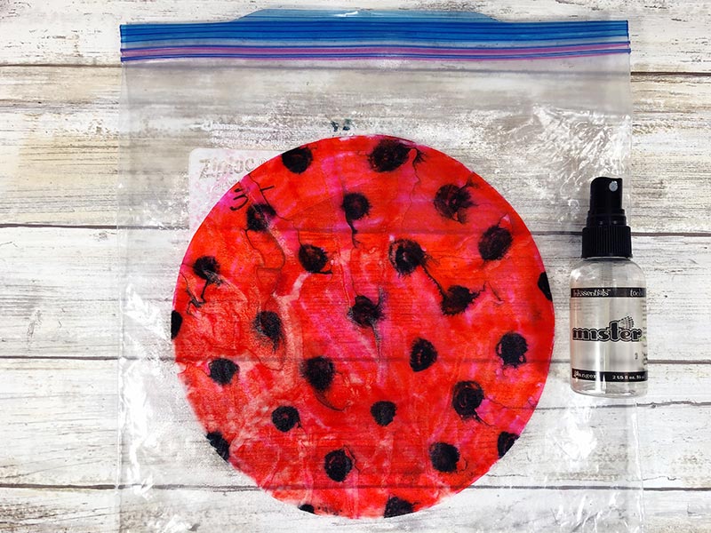 Wet red and black colored coffee filter laying on plastic bag next to water squirt bottle.