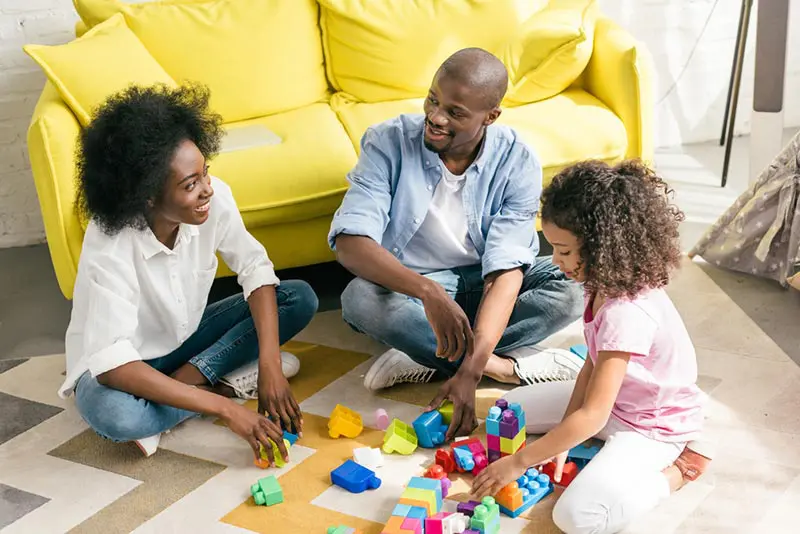 Happy Black family sitting on the floor together and playing with colorful blocks.