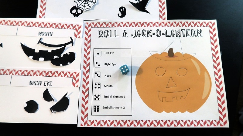 Roll a pumpkin printable page with hand drawn Jack-o-lantern face and blue die on black table.