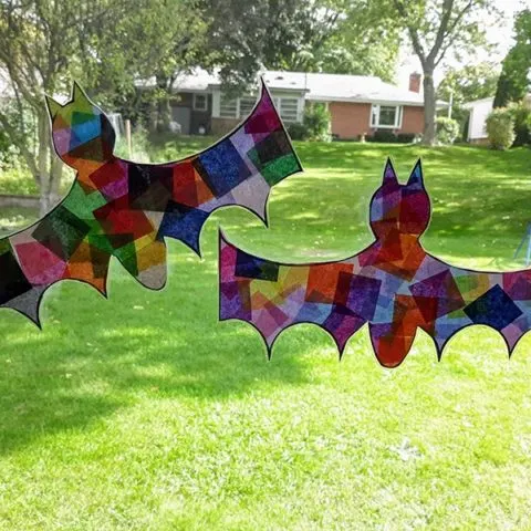 Two Halloween bat suncatchers made with tissue paper hanging in sunny window.