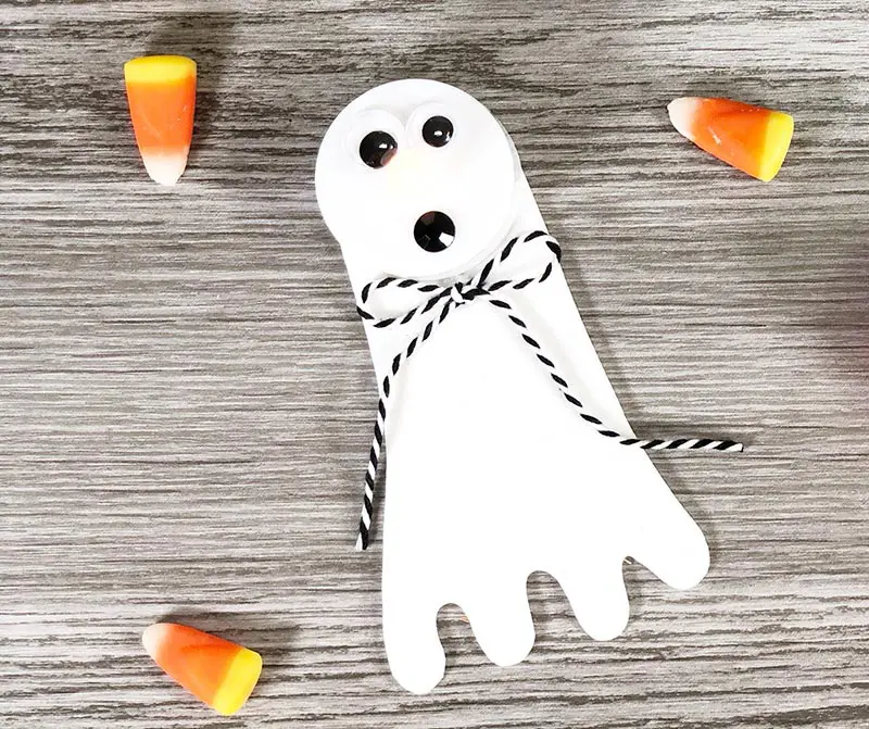 Overhead view of completed ghost tea light craft on gray wood background and three candy corn.