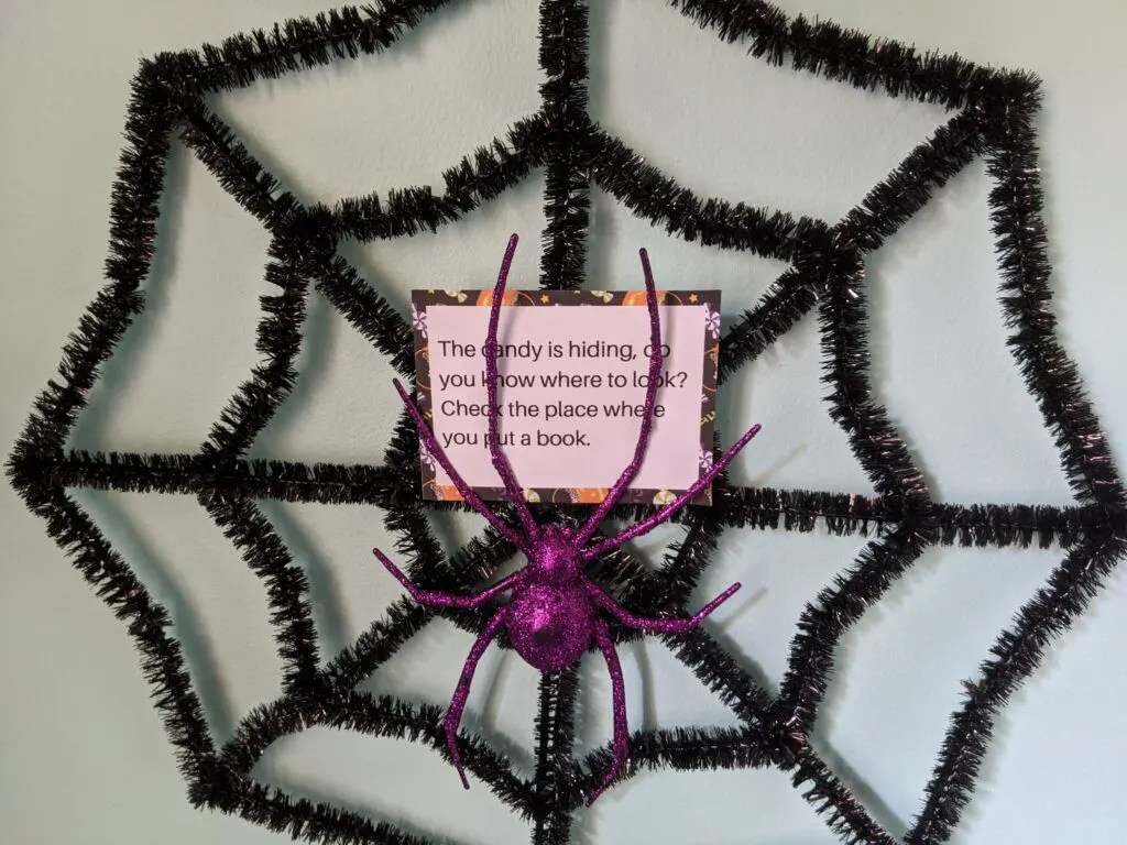 Halloween scavenger hunt riddle card hidden in a spider decoration on the wall.