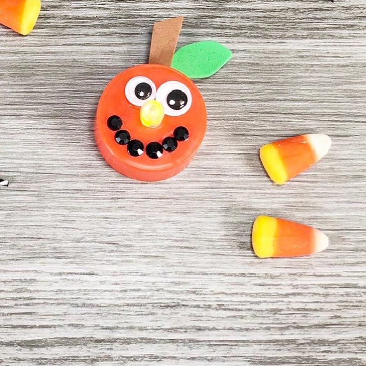 Finished Jackolantern pumpkin tea light craft with light on next to a couple pieces of candy corn on a gray wood background.