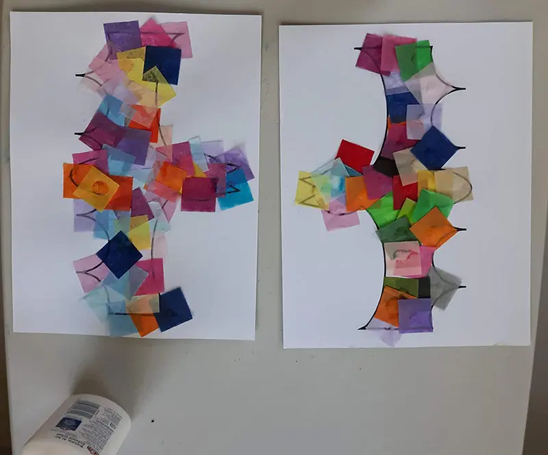 Overhead view of assorted colors of tissue paper squares glued to two print outs of bat template laying on table.