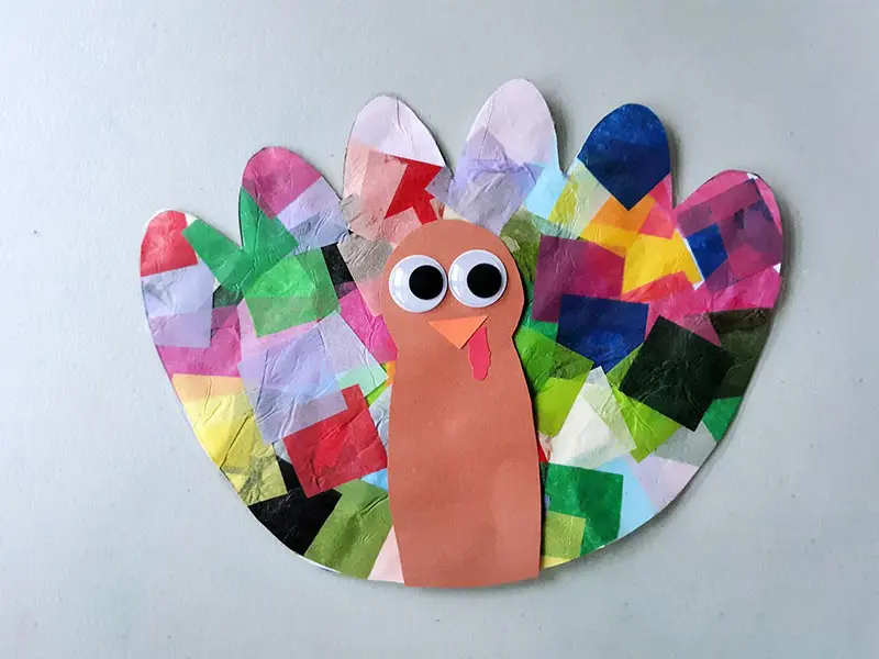 Completely assembled turkey tissue paper suncatcher craft laying on light gray table.