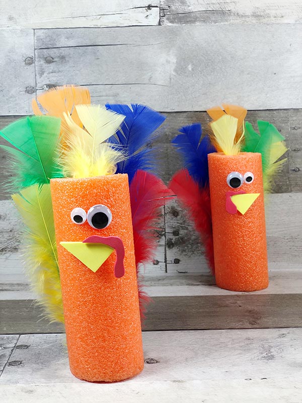 Two finished turkeys made out of orange pool noodles and different colors of craft feathers, one in the foreground and the other standing in the background.