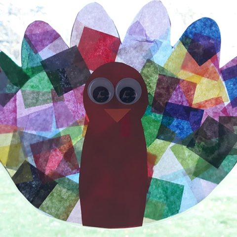 Turkey craft with tissue paper feathers and construction paper body hanging in window with sun shining through the feathers.