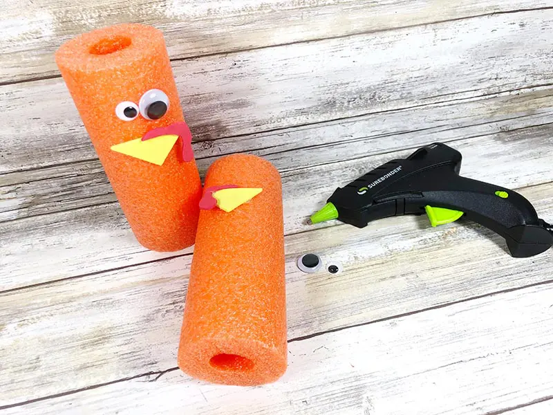 One orange pool noodle with turkey face standing up. Another piece of orange pool noodle laying on its side with yellow beak hot glued on.