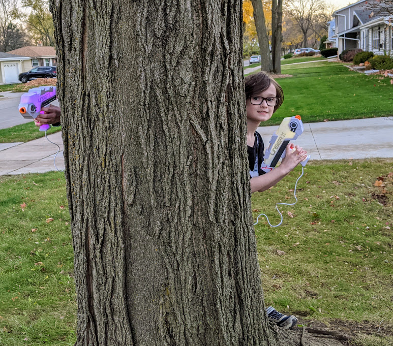 White boy holding Laser X Revolution Blaster while standing behind a tree.