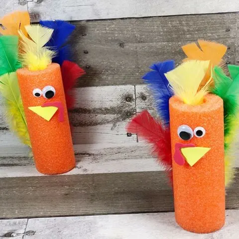 Two orange pool noodle turkeys standing on a gray wood background.