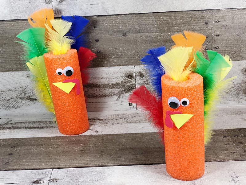 Two orange pool noodle turkeys standing on a gray wood background.
