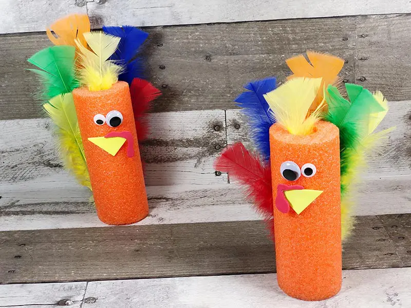 Two orange pool noodle turkeys standing on a gray wood background.