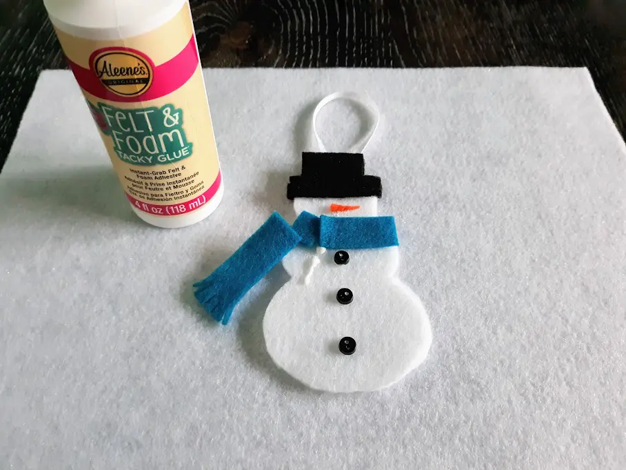 Gluing blue felt pieces to make scarf on snowman ornament