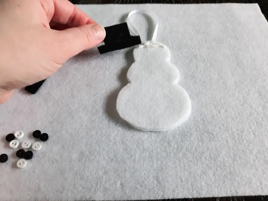 White woman's hand gluing black felt hat to felt snowman's head.