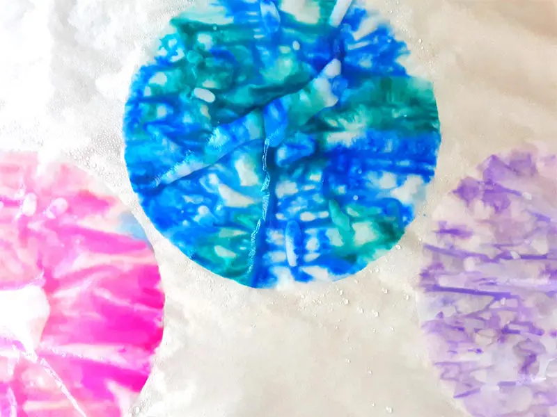 Three wet coffee filters with marker colors blending together. Filter on left is bright pink, middle filter is blue and green, and right filter is light purple.