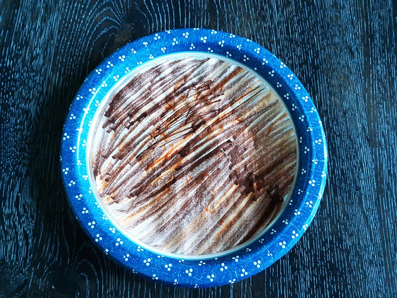 Overhead view of a round coffee filter colored with brown and yellow markers on a paper plate with blue border on a table.