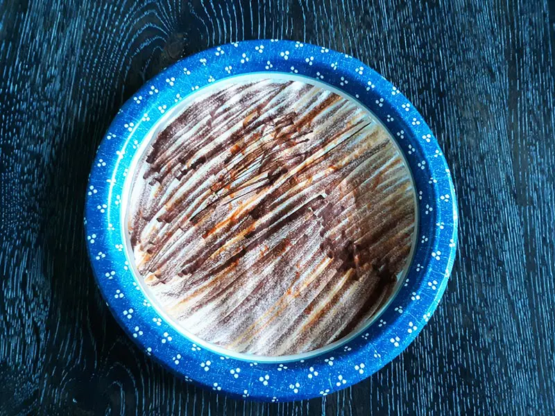 Overhead view of a round coffee filter colored with brown and yellow markers on a paper plate with blue border on a table.