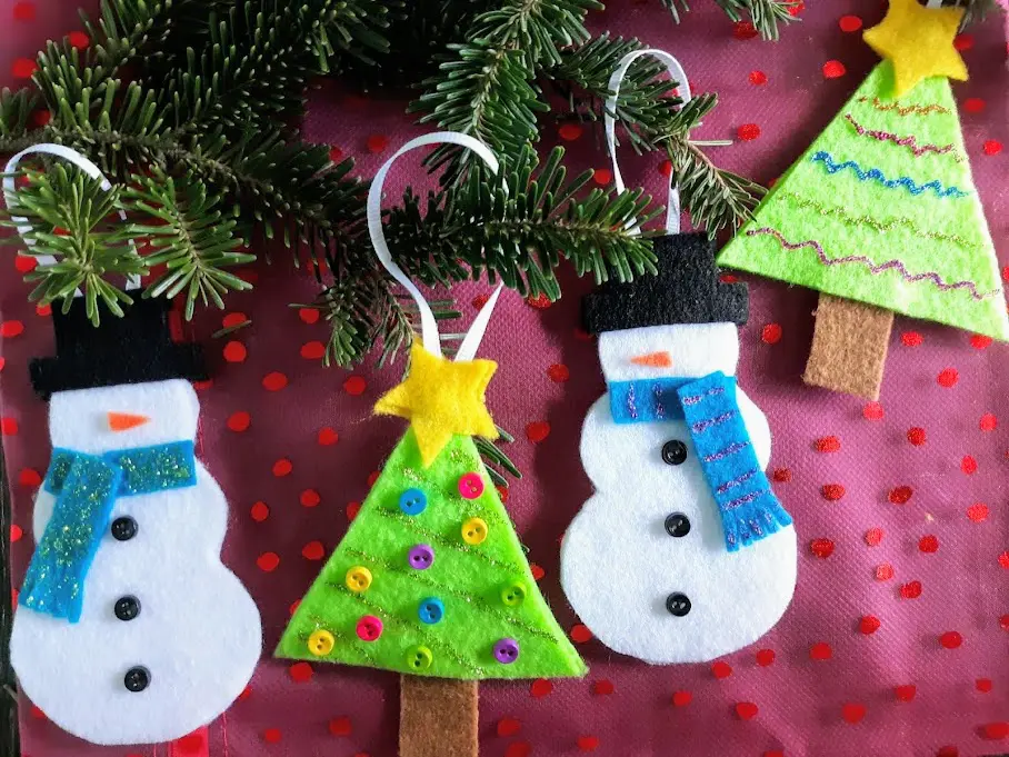 Two felt snowmen and two felt Christmas trees ornaments alternating in a row. Ribbon loops on evergreen branches with a red background.