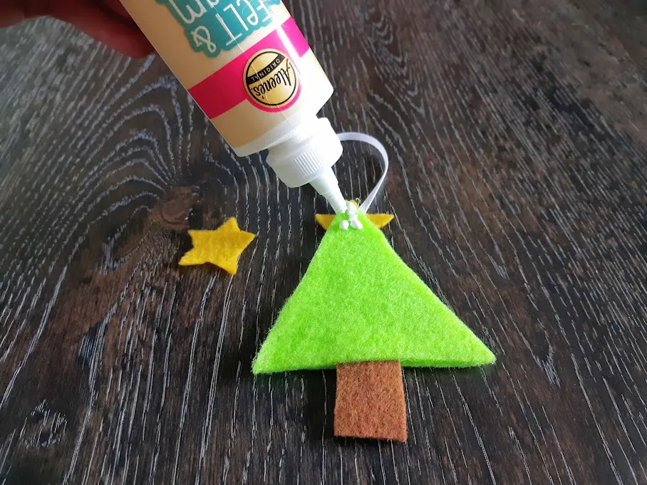 Using felt and foam tacky glue to attach yellow felt star to top of felt Christmas tree ornament.