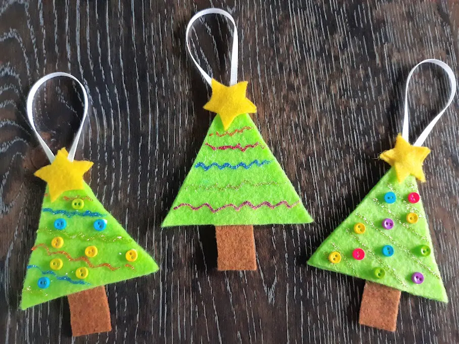Three complete felt Christmas tree ornaments laying in a row on a dark wooden table.