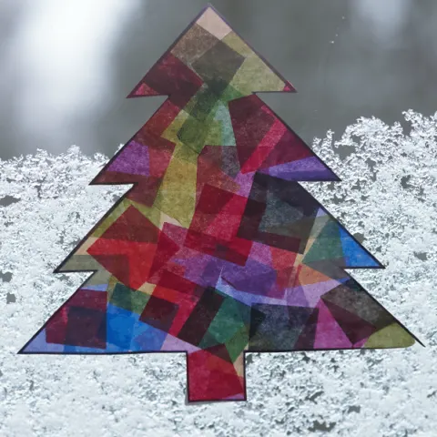 Close view of completed Christmas tree suncatcher hanging on snowy window.