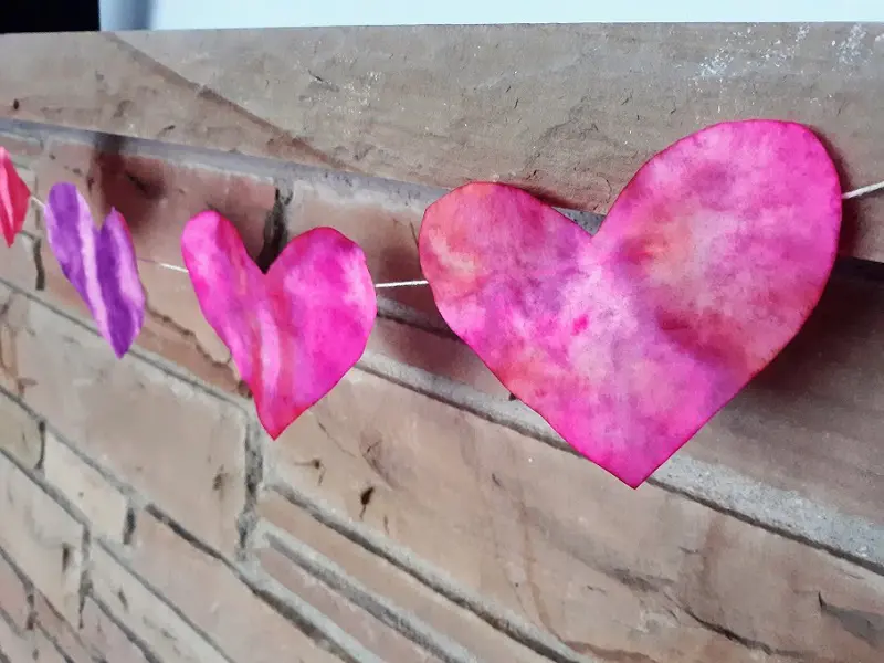 Pink and purple colored coffee filter hearts strung up as garland using twine on a brick mantel.