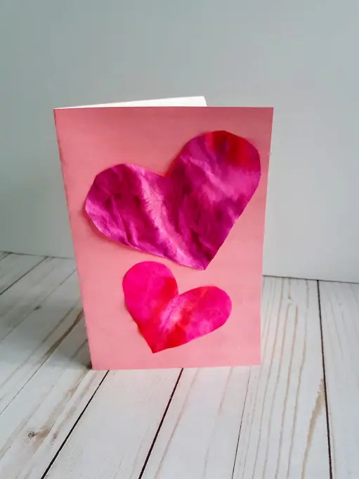 Homemade valentine card made with pink card stock and two different sized coffee filter hearts glued to the front.