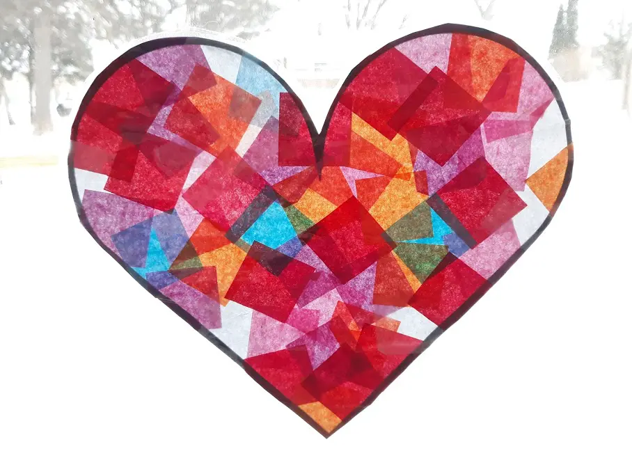 Completed heart suncatcher made with red, pink, purple, white, blue, and orange tissue paper and hung in a brightly lit window.