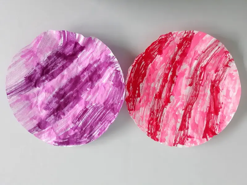 One round coffee filter colored with purple and pink markers laying next to another colored with red and pink markers.