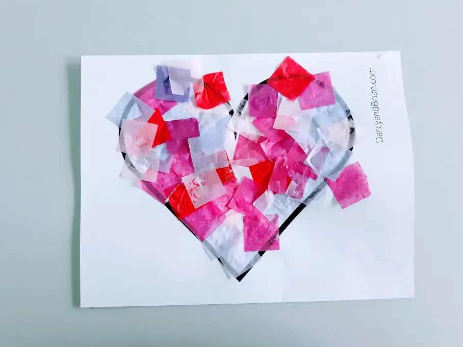 Overhead view of heart template covered with glued on tissue paper squares.
