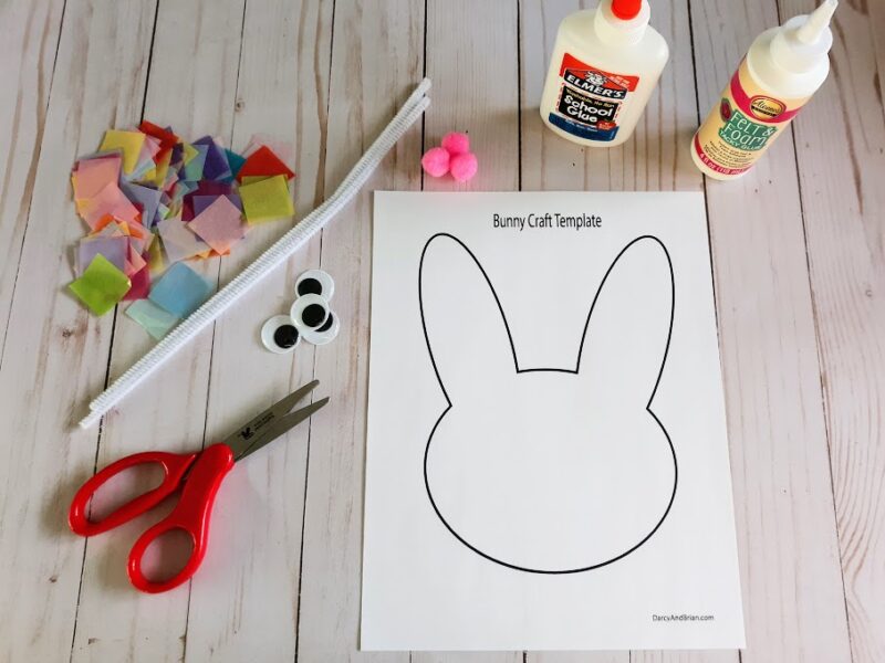 Overhead view of bunny template printed out and laying next to glue bottles, pom poms, tissue paper squares in a variety of colors, white chenille stem, googly eyes, and scissors with red handles.