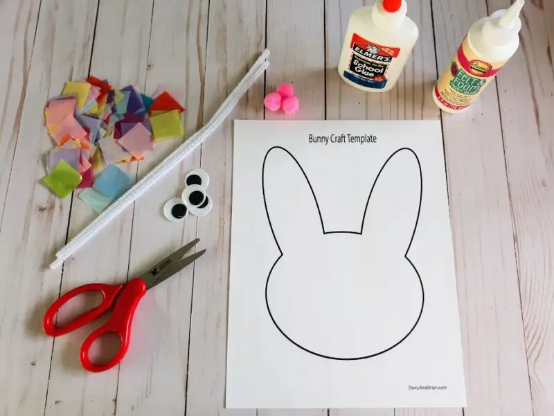 Overhead view of bunny template printed out and laying next to glue bottles, pom poms, tissue paper squares in a variety of colors, white chenille stem, googly eyes, and scissors with red handles.