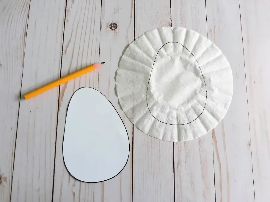 Cut out egg craft template next to a pencil and a coffee filter with traced egg shape drawn on it.