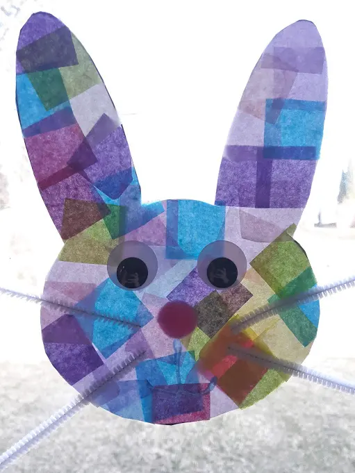 Tissue paper bunny suncatcher with eyes and whiskers in a brightly lit window, sun showing through it.