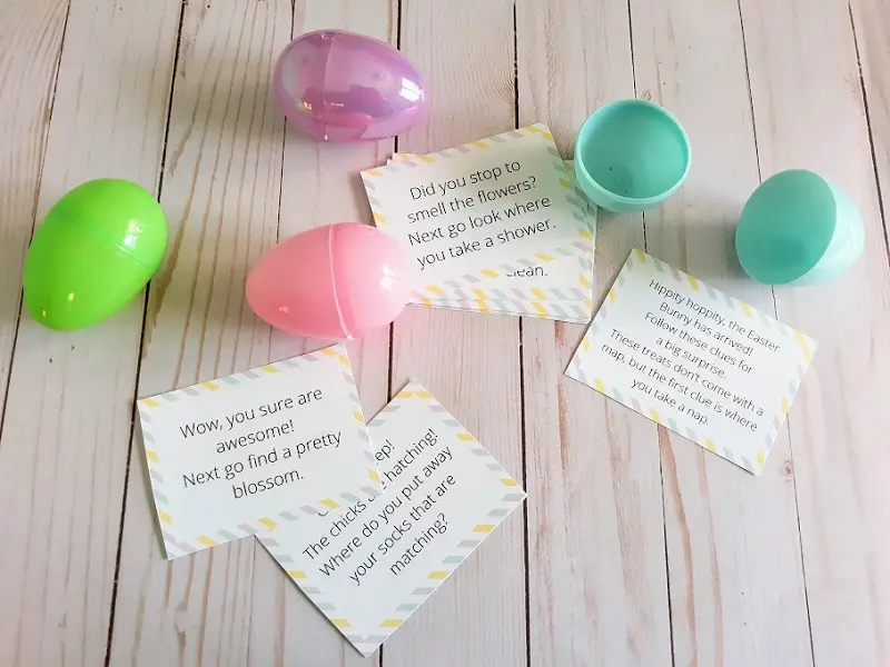 Five Easter scavenger hunt clues cut out and laying by three closed plastic Easter eggs and one open plastic egg in various colors.