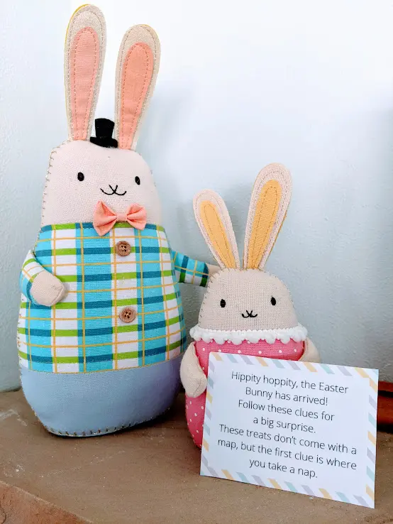 Easter scavenger hunt clue propped up next to decorative spring bunnies wearing clothes.