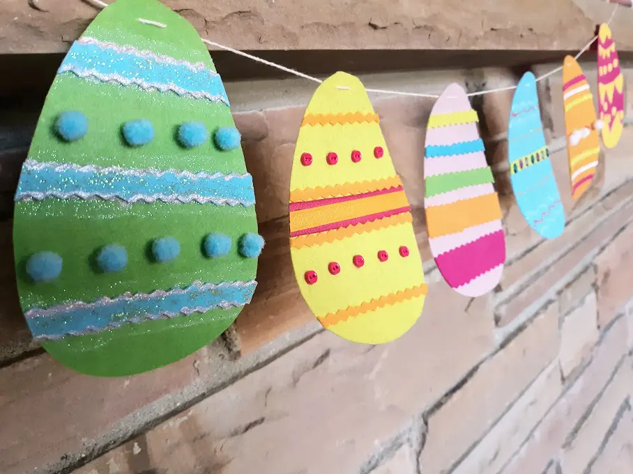 Multicolored felt eggs strung as a banner across a brick mantle.